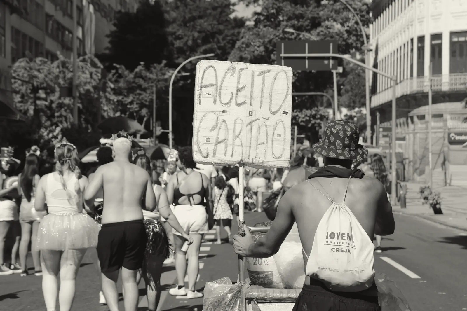 Vendedor ambulante de costas, com uma placa “Aceito cartão”, no meio de um bloco de carnaval no Rio.